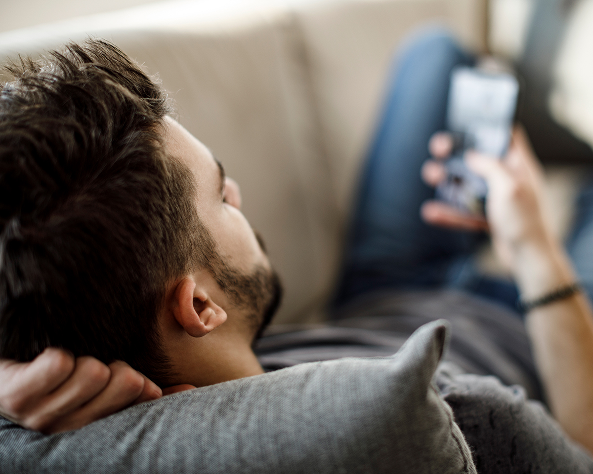 Man laying on couch looking at cell phone