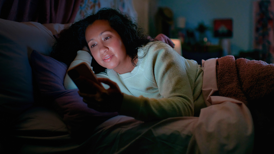 woman laying on her couch in the dark on her phone