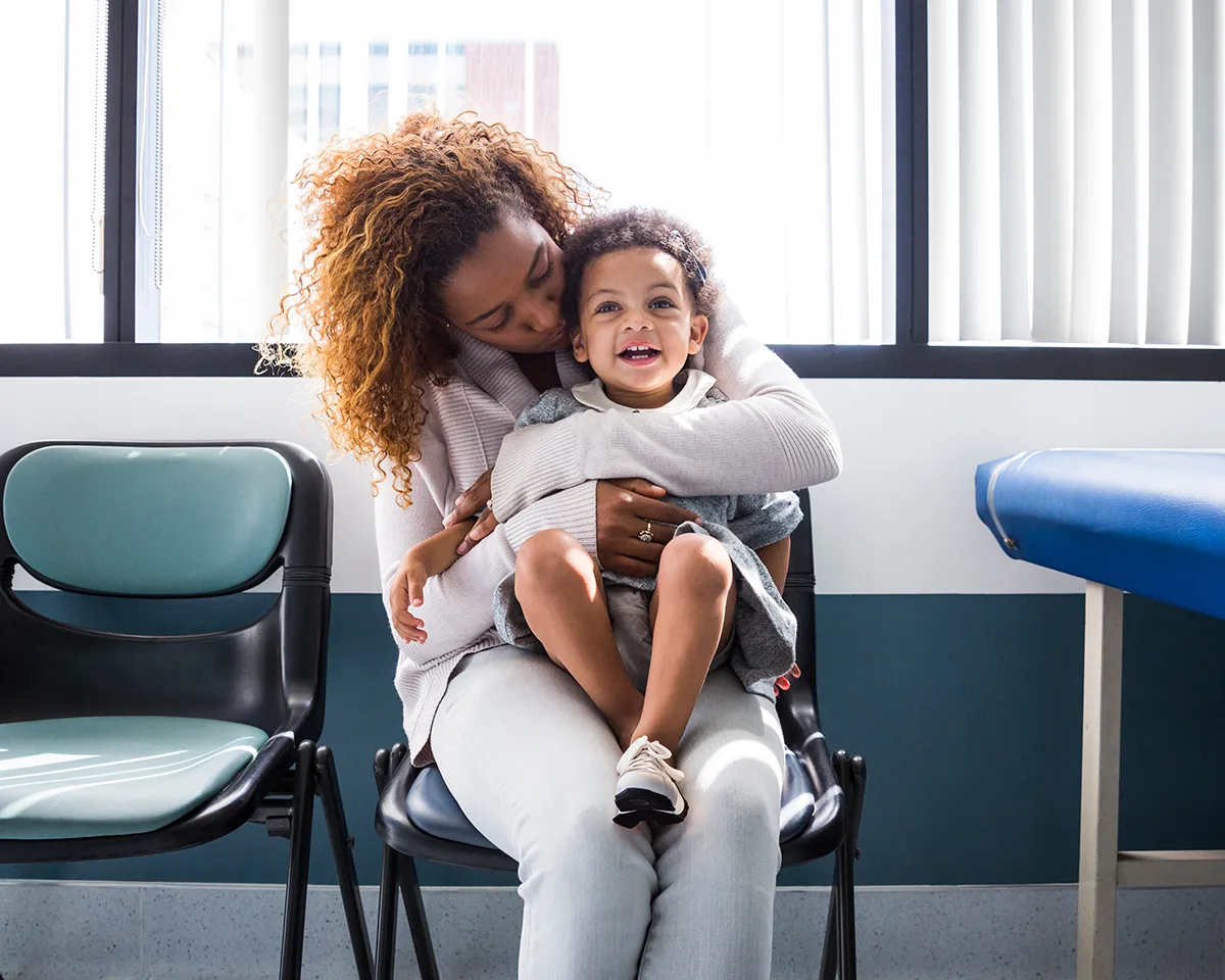 Woman sitting in doctor's office hugging her toddler on her lap