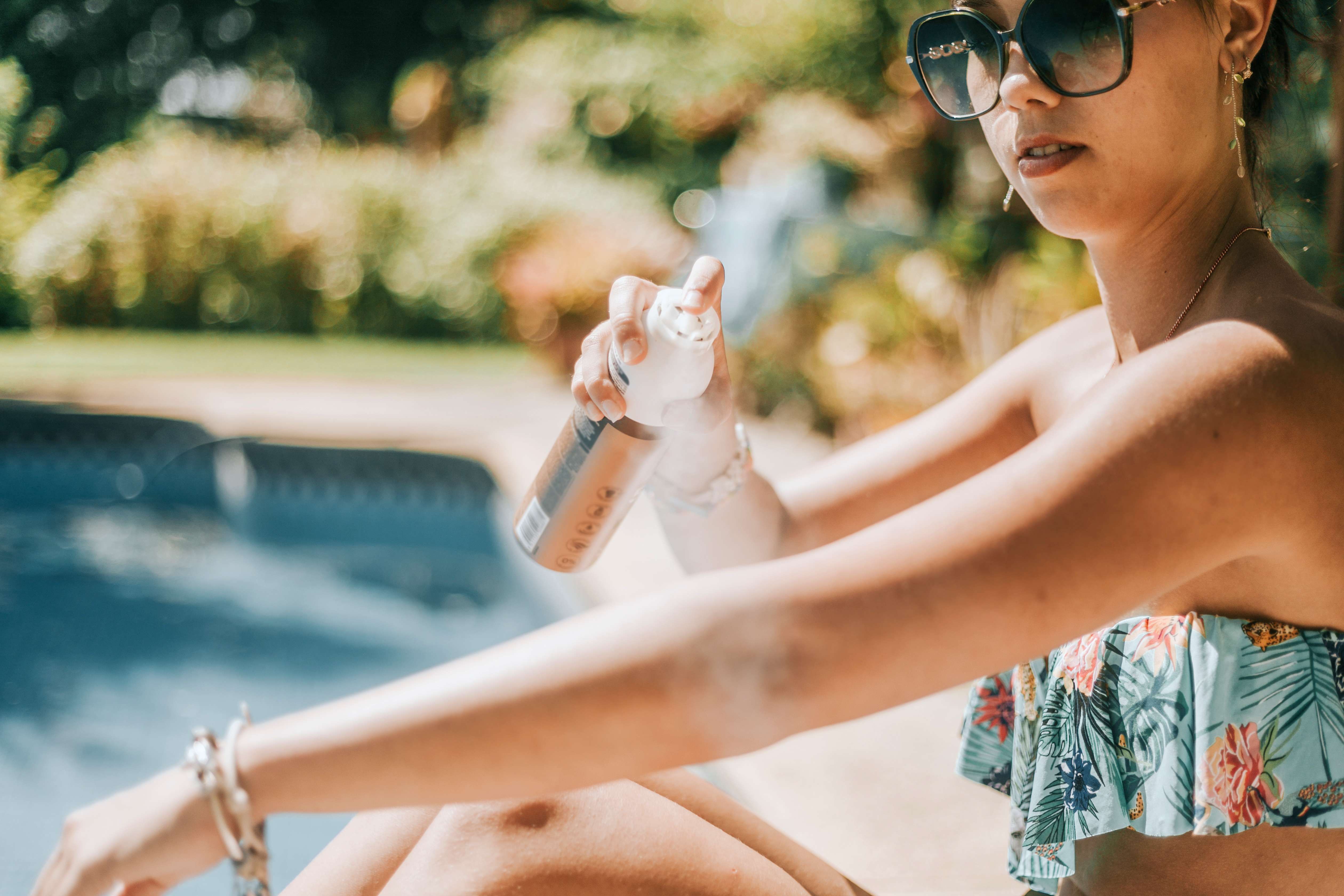 Woman putting sunscreen on her arm sitting by a pool.